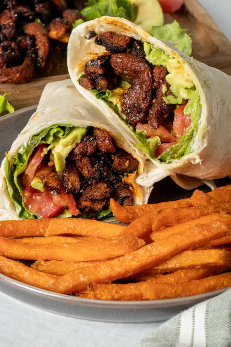 Wrap cut in half and stacked with fries in front of it on a plate.