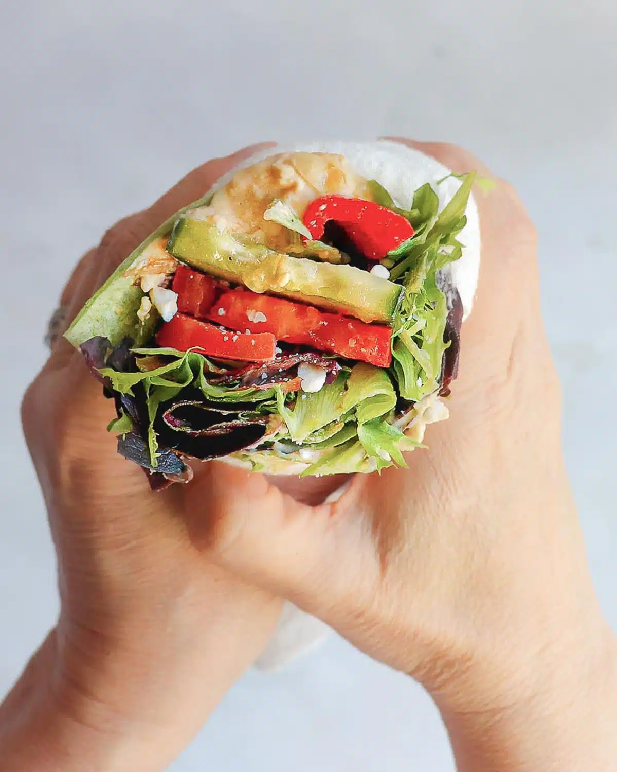 A Mediterranean wrap with hummus, cucumbers, and feta, held close to the camera.