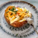Loaded baked potato on a blue plate with a fork.