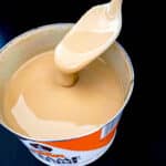 A spoon with tahini sauce dripping off of it.