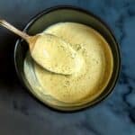 Lemon herb tahini sauce dripping off of a spoon.
