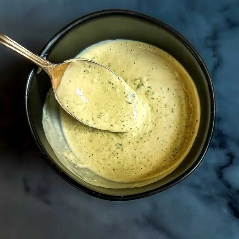 Lemon herb tahini sauce dripping off of a spoon.