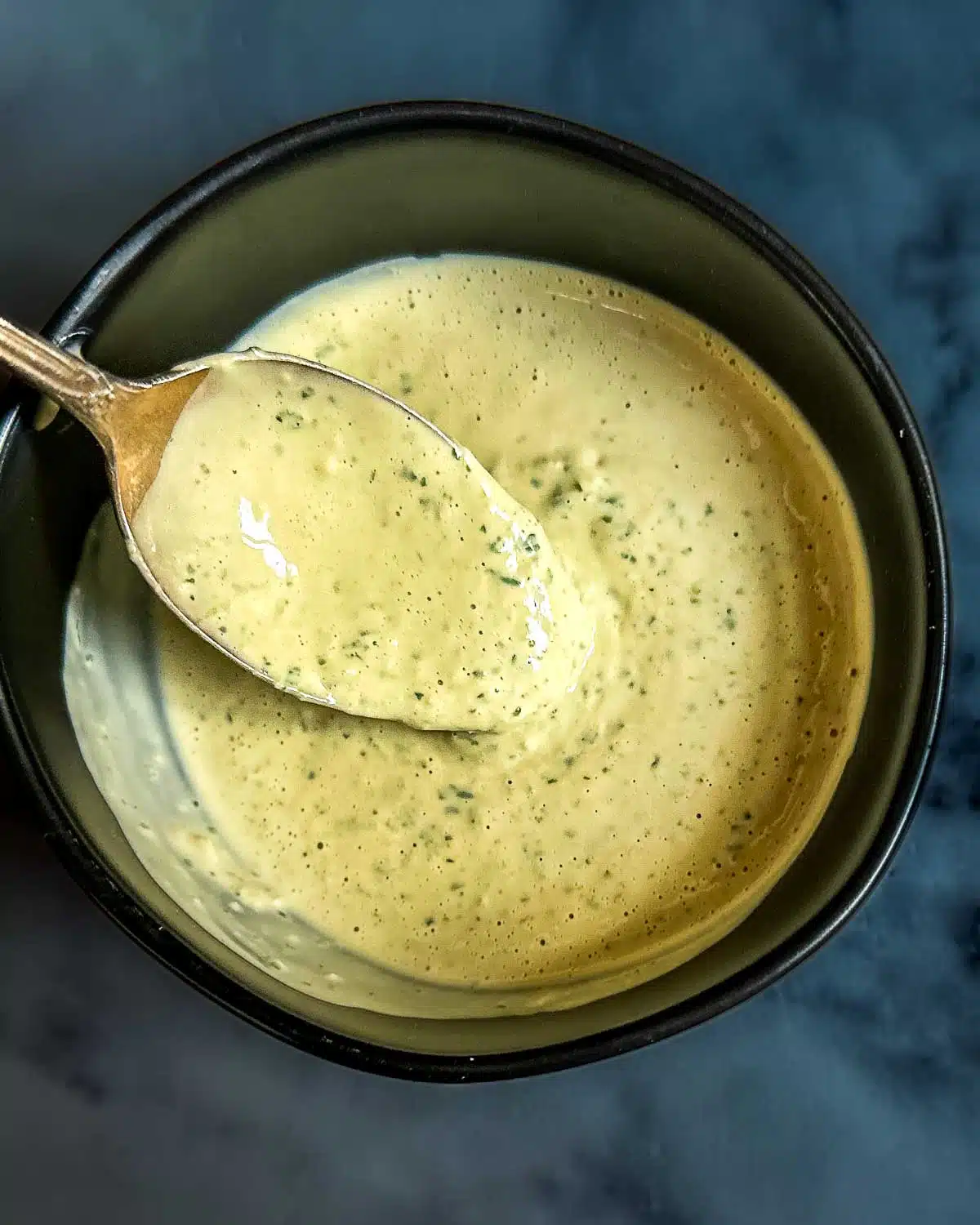 Lemon herb tahini sauce dripping off of a spoon. 