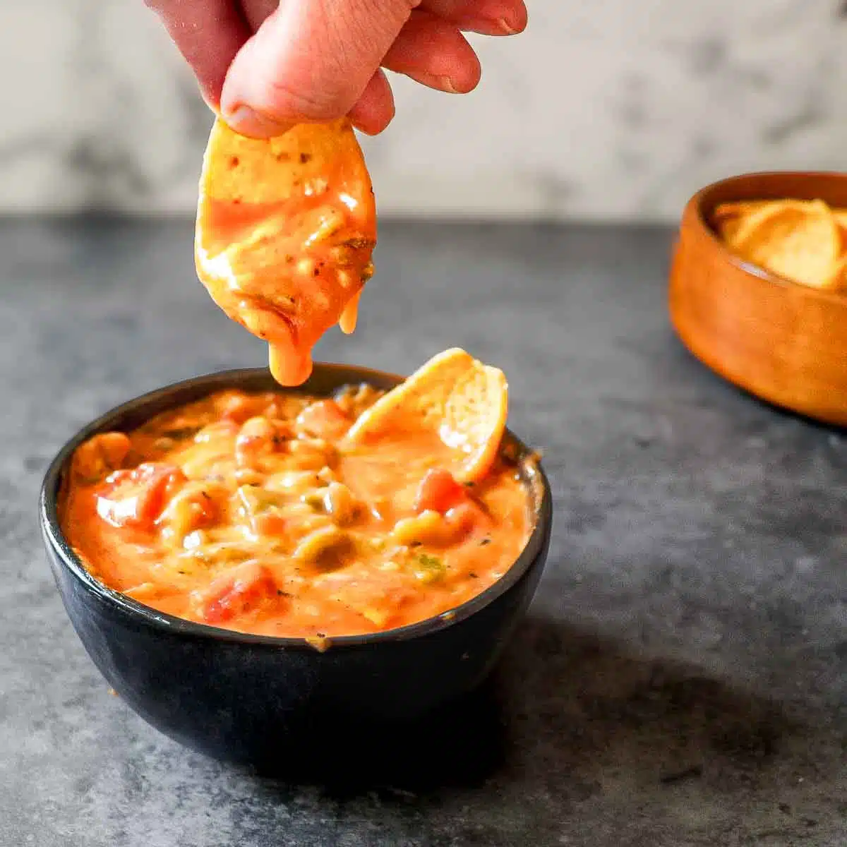 Hand holding a Frito dipping a chip into a cheese green chile dip.