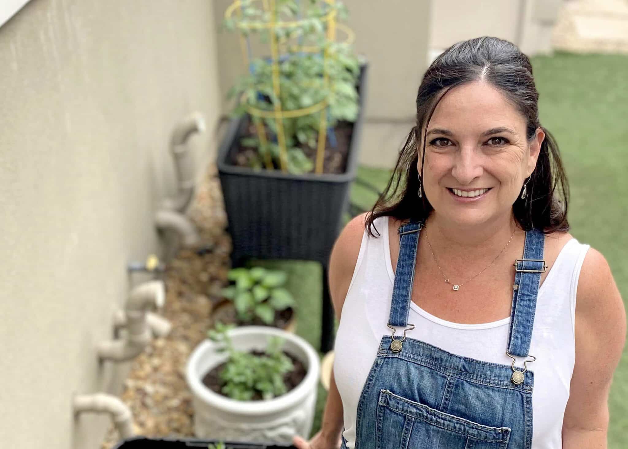 A picture of Ruth in overalls standing next to her little townhome container garden.