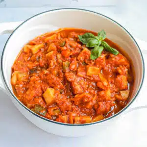 A Dutch oven filled with Ciambotta garnished with a basil leaf.