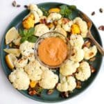 Roasted cauliflower dipped in tahini sauce held up to the camera.