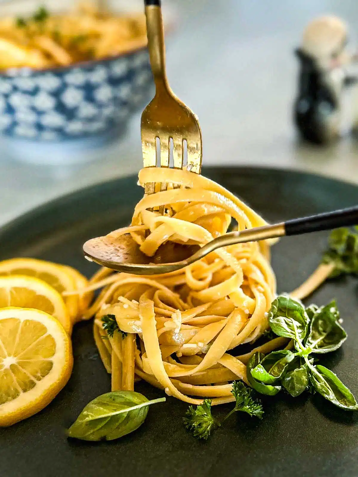 Thick linguini lemon pasta noodles wrapped around a fork. Garnished with basil leaves, parsley lemon and cheese.