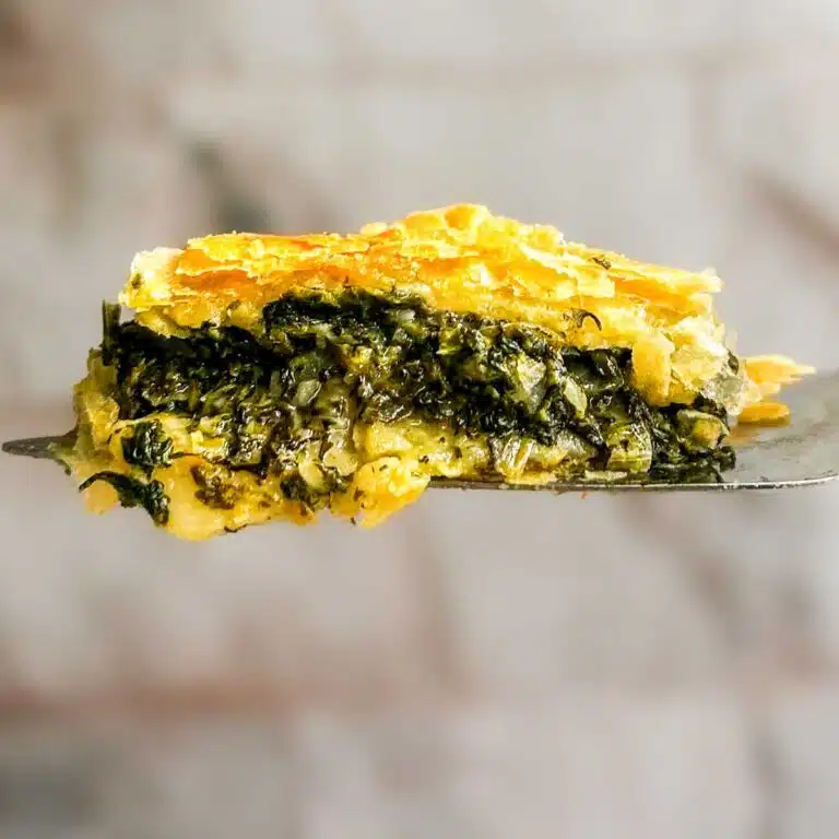 A square of puff pasty spanakopita on a serving spoon.