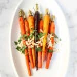 Harissa carrots on a plate garnished with almonds and parsley.