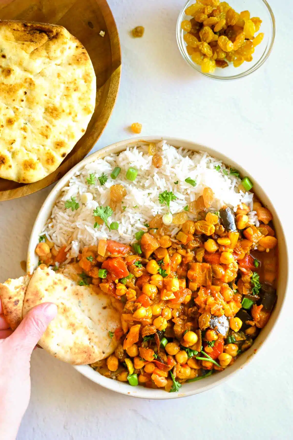 A bowl filled with chickpea tagine, rice, and a hand with nann bread scooping up a bite. 