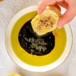 Hand dipping bread into olive oil and vinaigrette.