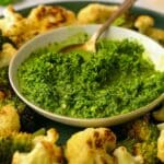 A bowl of green harissa surrounded by roasted cauliflower.