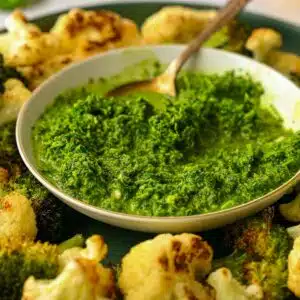 A bowl of green harissa surrounded by roasted cauliflower.