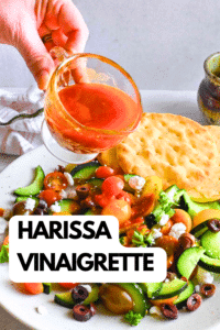 Pouring harissa vinaigrette onto a salad.