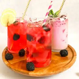 Three glasses each filled with a variation of the blackberry refresher. One mixed with water, another with lemonade, and the midnight mixed with coconut milk.