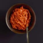 Harissa paste in a small bowl with a spoon in the bowl.