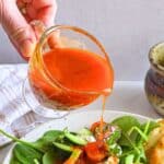 Harissa Vinaigrette being poured onto a salad.