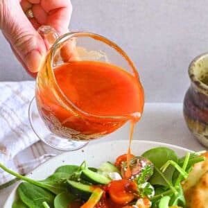 Harissa Vinaigrette being poured onto a salad.