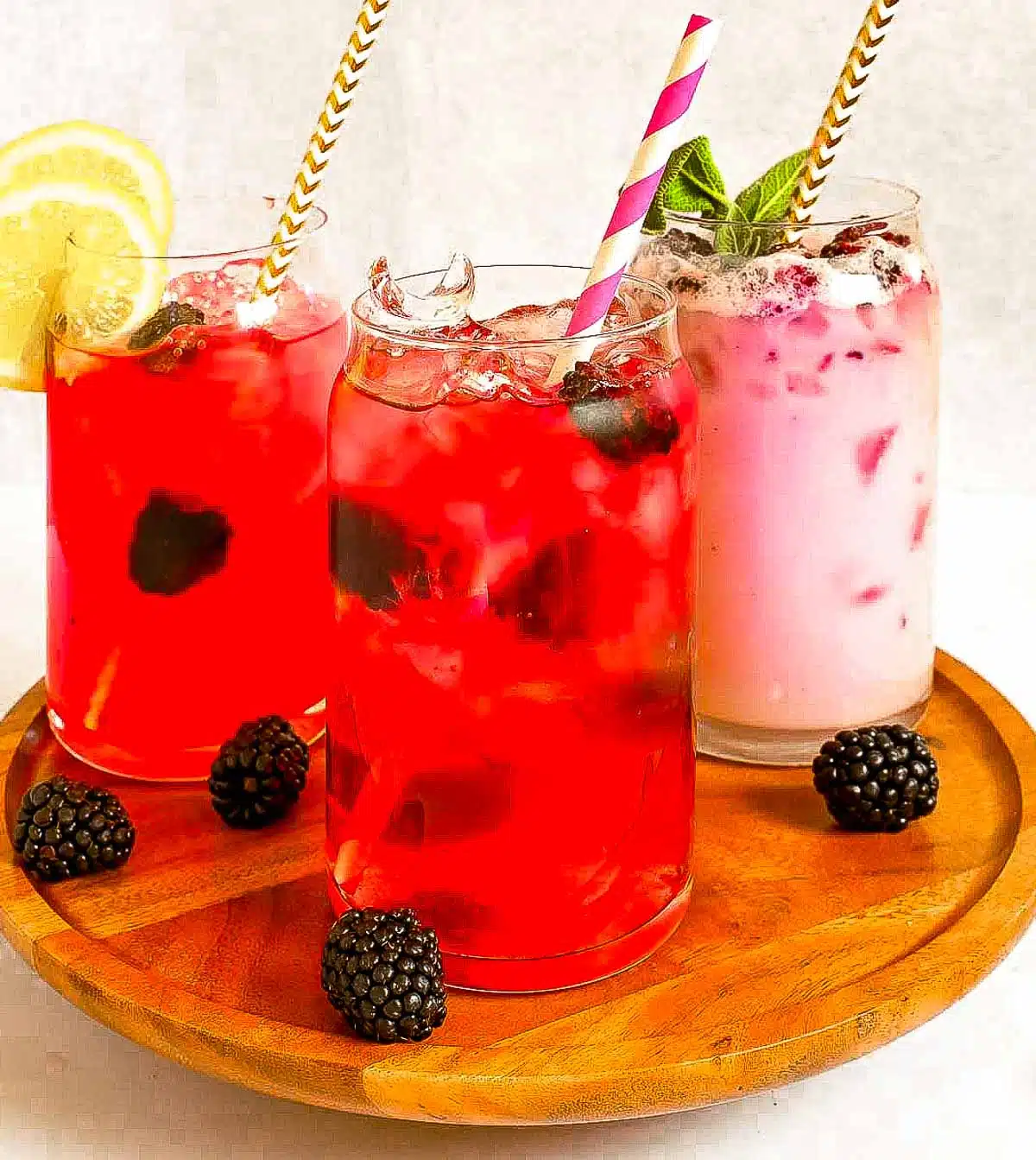 Three glasses each filled with a variation of the blackberry refresher.  One mixed with water, another with lemonade, and the midnight mixed with coconut milk. 