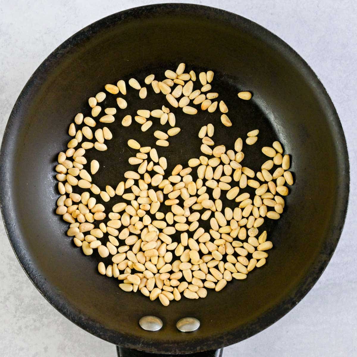 Toasted pine nuts in a small skillet.