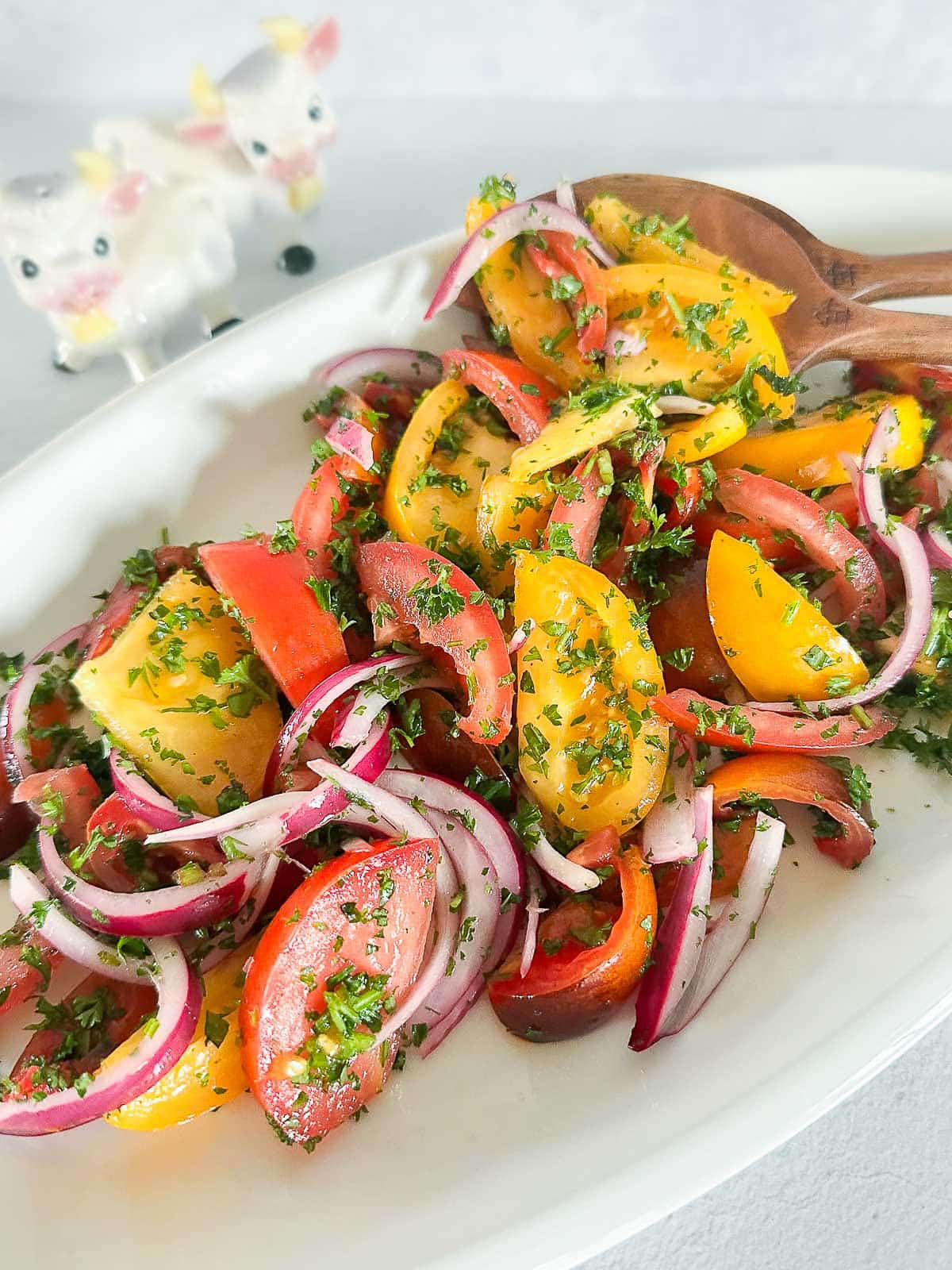Mediterranean tomato and onion salad on a long plate with wooden spoons.