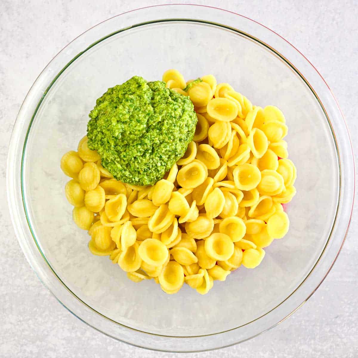 Cooked pasta in a bowl with lemon pesto on top, but not yet mixed in.