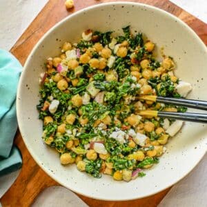 Kale garbanzo bean salad topped with feta cheese in a large bowl on top of a serving platter.