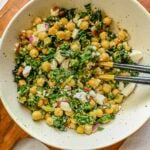Kale and garbanzo bean salad in a white stone bowl with two forks inside the bowl.