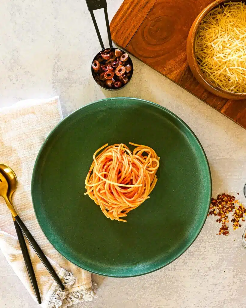 Spicy pasta on a plate with crushed red peppers near the plate.