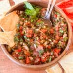 Turkish tomato and pepper dip in a bowl with pita chips near it.