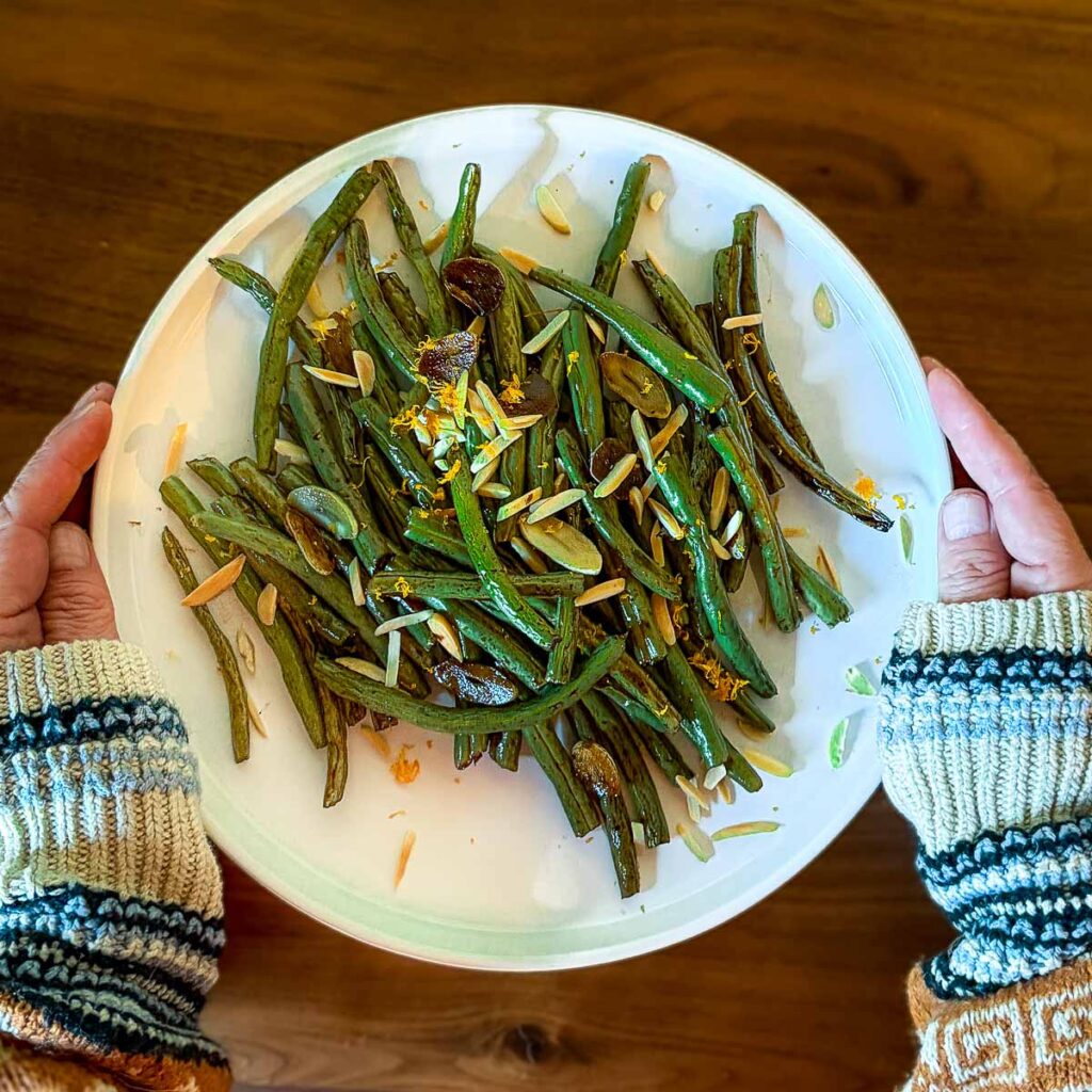 A plate filled with balsamic green beans topped with pine nuts and orange zest.