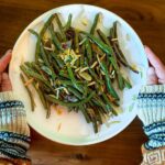 A plate filled with balsamic green beans topped with pine nuts and orange zest.