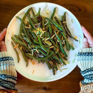 A plate filled with balsamic green beans topped with pine nuts and orange zest.