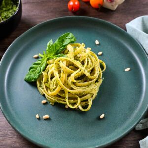 Pesto pasta on a plate with pine nuts and basil on the plate.