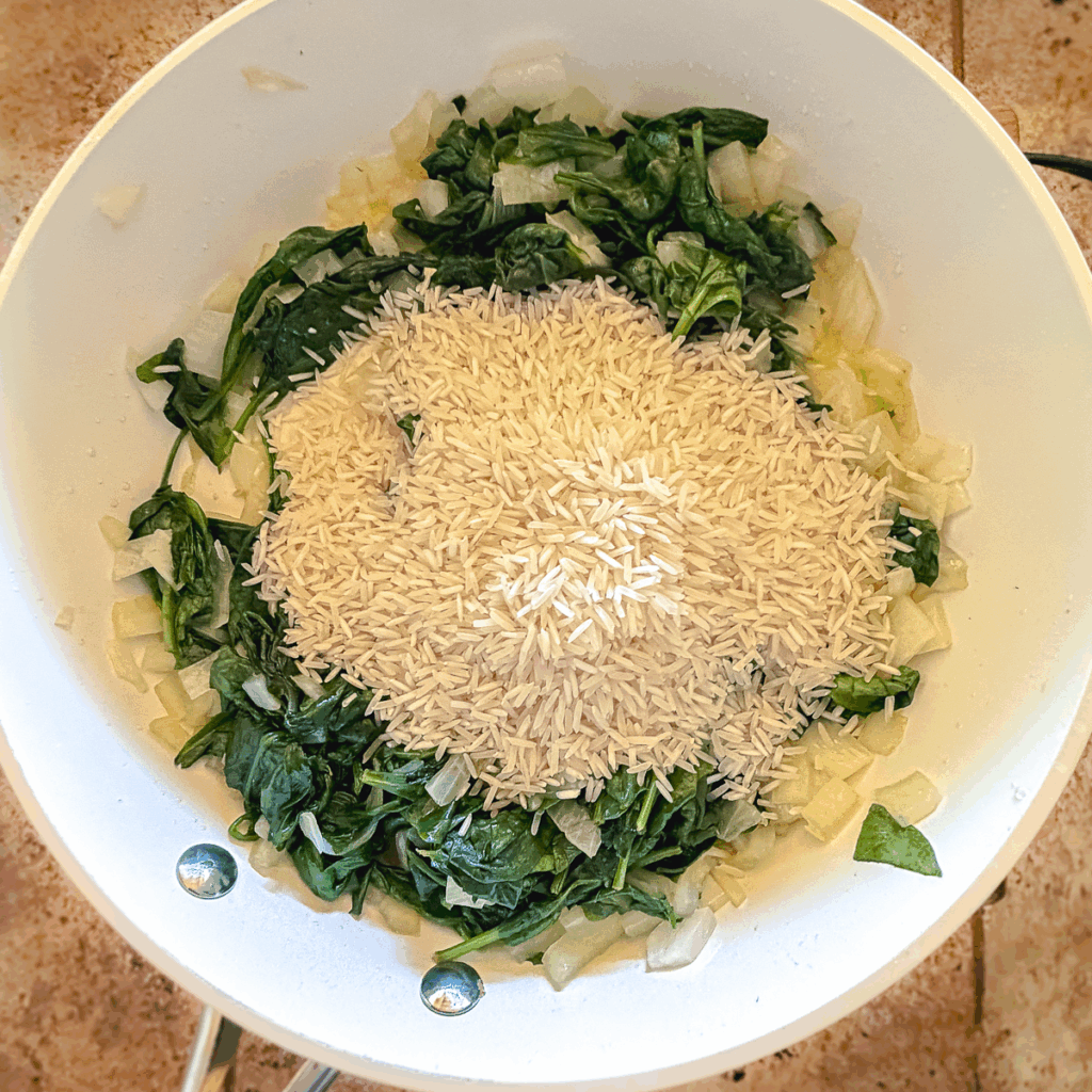Adding basmati rice to a skillet with onions and spinach.