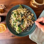 A hand holding a spoon on a green plate scooping up Greek spakakorizo.
