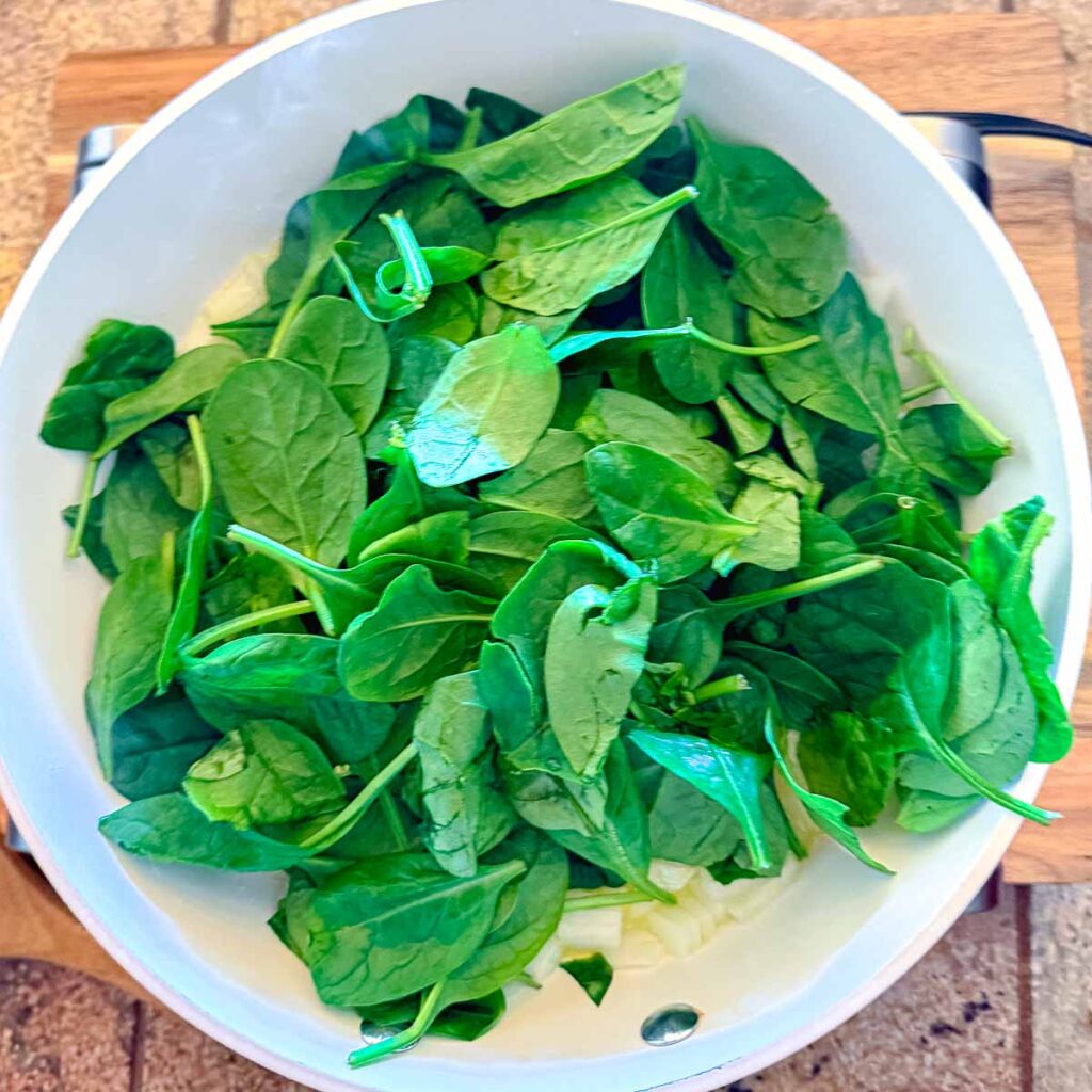 A batch of spinach added to the skillet to make Greek spinach rice.