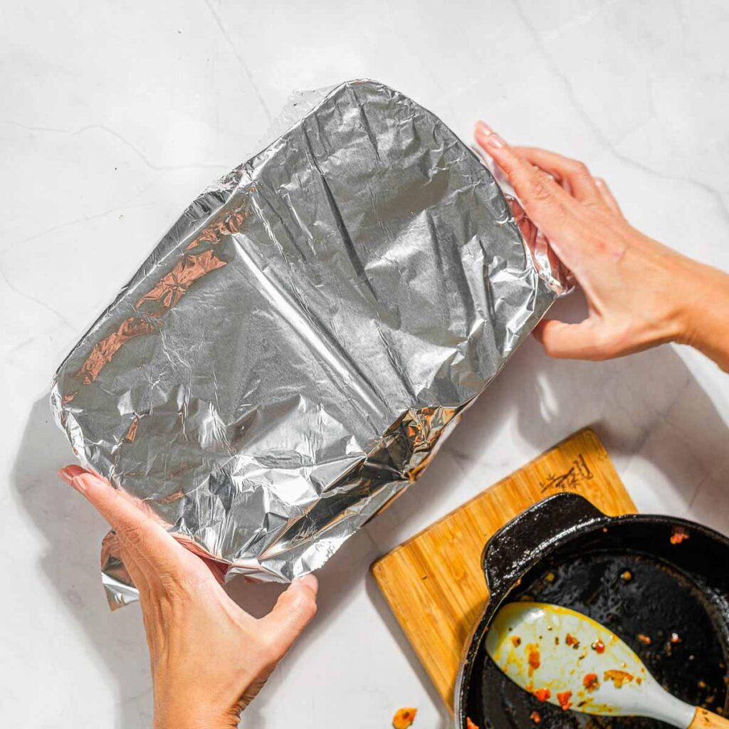 Placing foil over a casserole dish filled with stuffed eggplants.