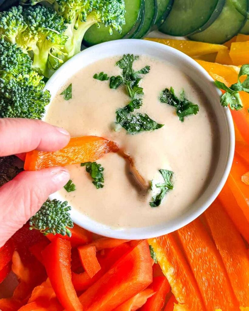 Dipping an orange bell pepper into a bowl filled with tahini sauce.