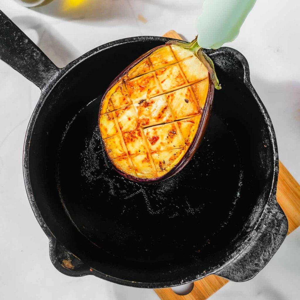 A tong holding up a sautéed eggplant.