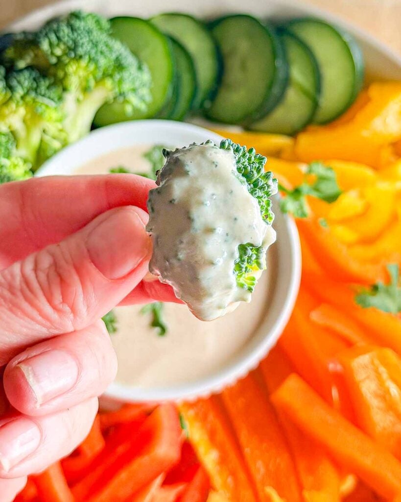 Hand holding broccoli that has been dipped into tahini sauce up close to the camera.