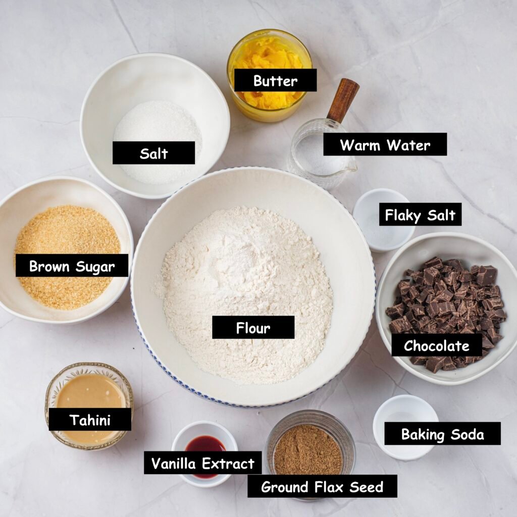 Ingredients used in making vegan tahini cookies with chocolate chips: tahini, flour, brown sugar, ground flax seed, vanilla extract, salt, flaky salt, baking soda, butter, warm water, and chocolate.)