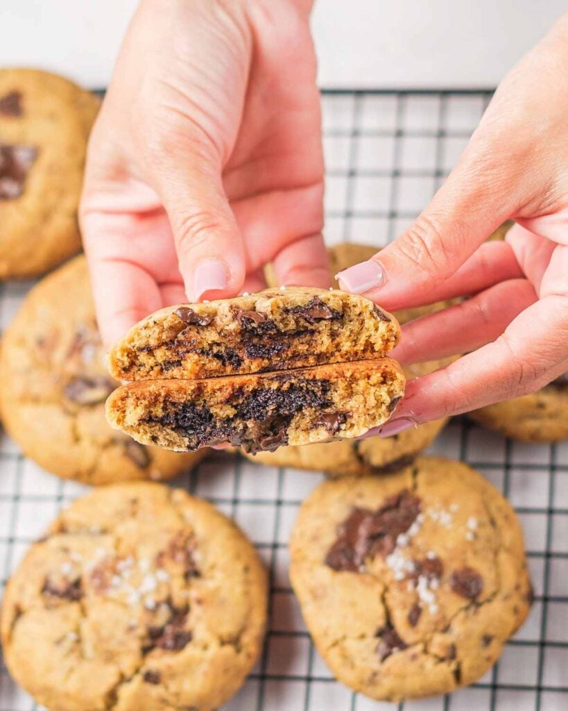 A hand holding a vegan tahini cookie that has been bent in half exposing the melty chocolate chunks.