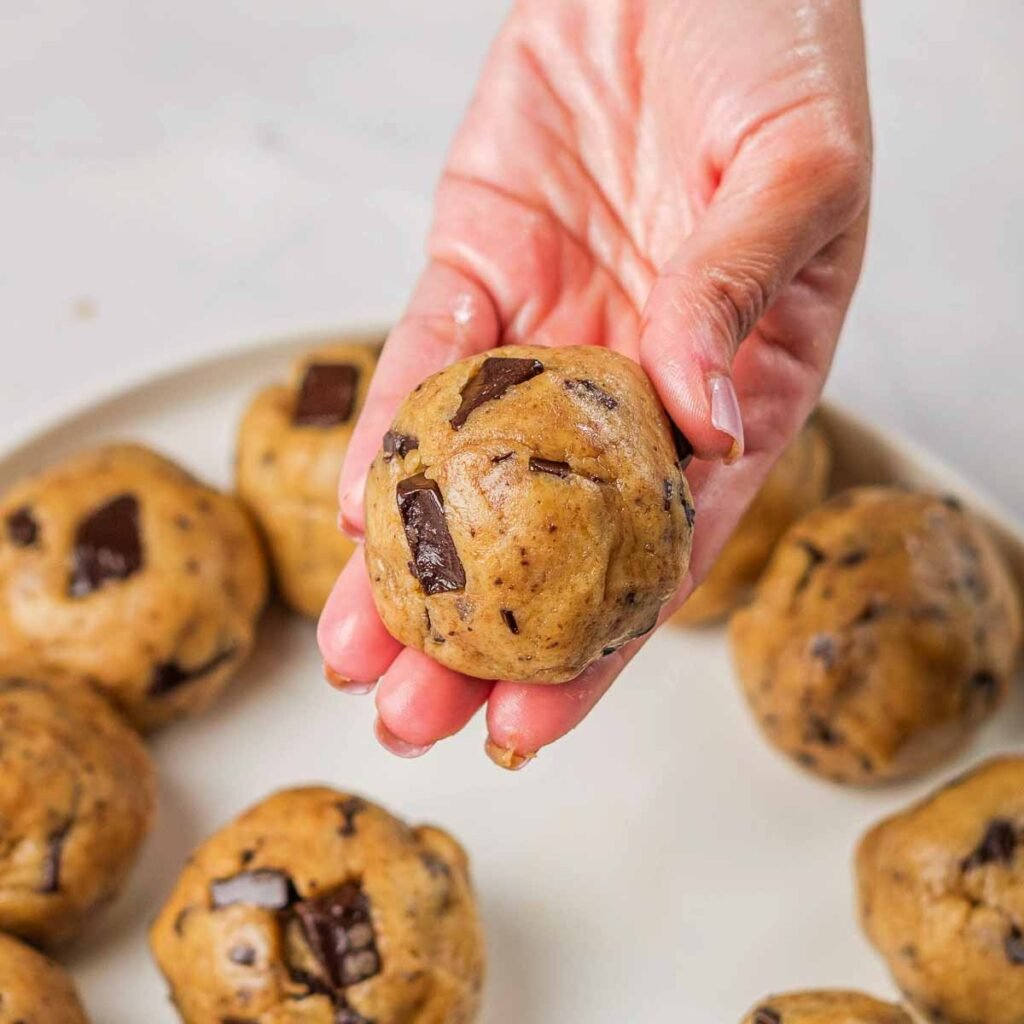 A hand holding a ball of vegan cookie dough up to the camera.