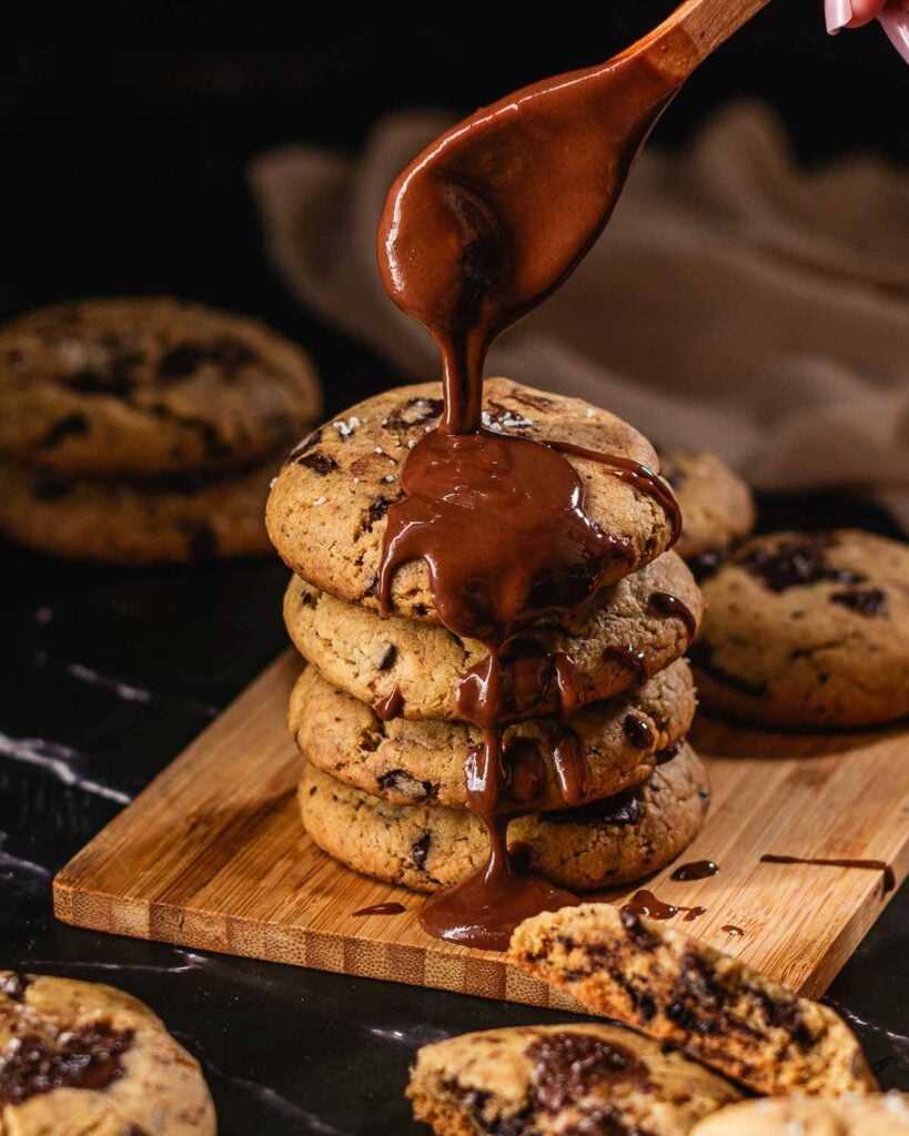 Drizzling chocolate on top of a stack of vegan tahini cookies.