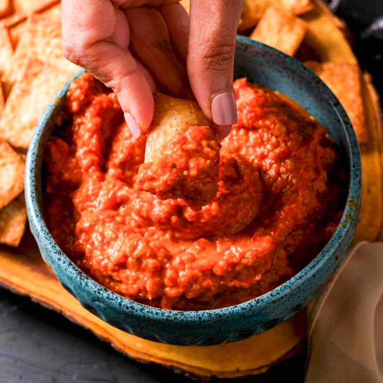 A hand dipping a chip into roasted red pepper and eggplant dip.