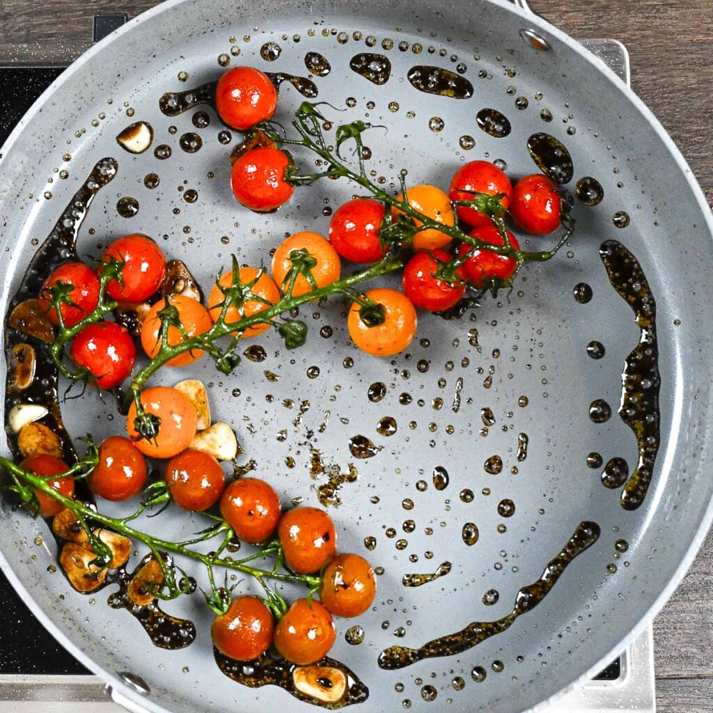 Cherry tomatoes on the vine in a skillet with olive oil in the early stages of blistering.
