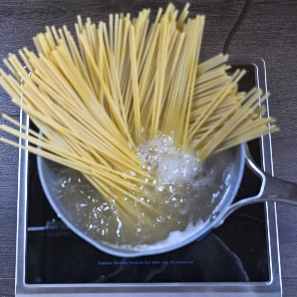 Bucatini pasta noodles that have just entered boiling water.