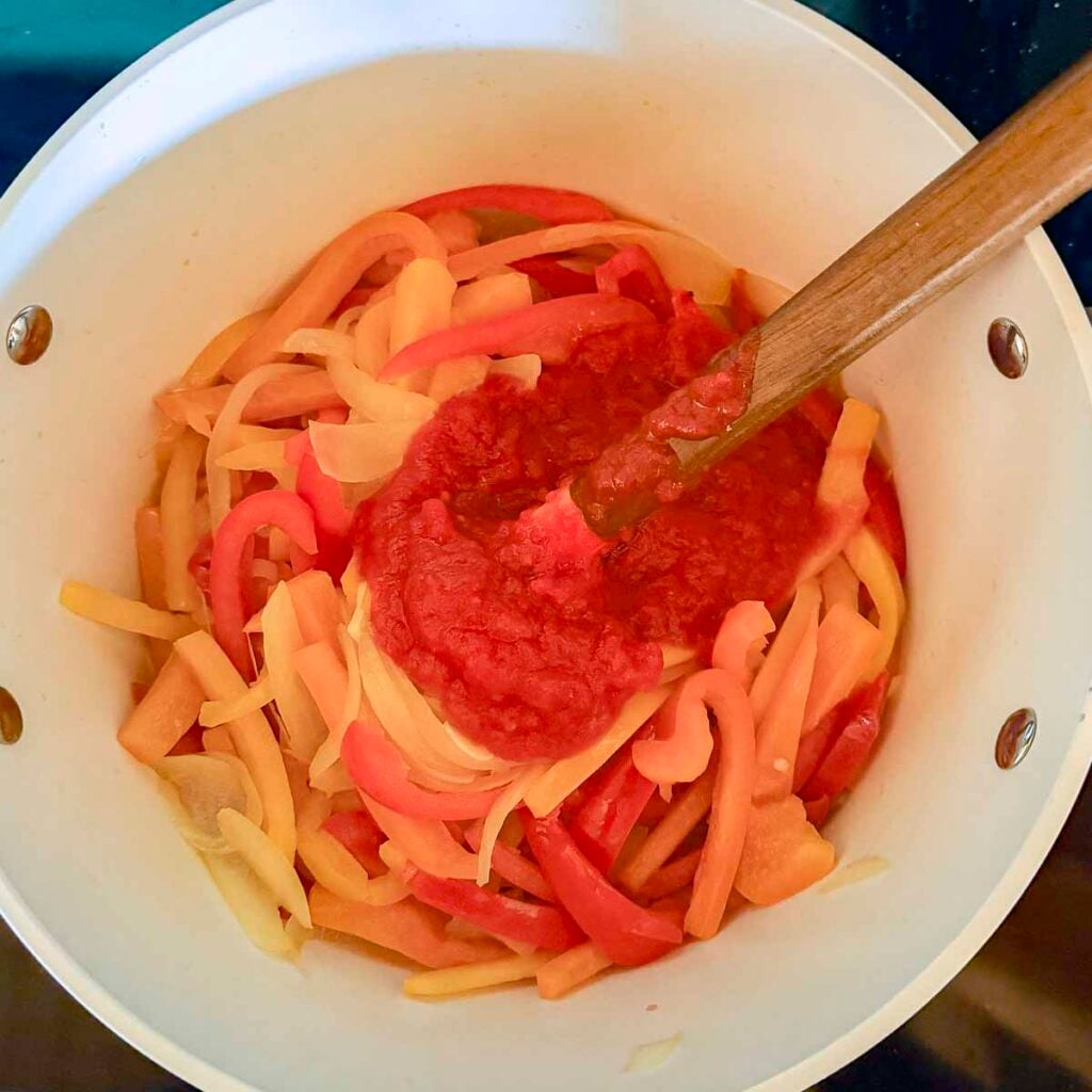 Peperonata in a saucepan with crushed tomatoes added.
